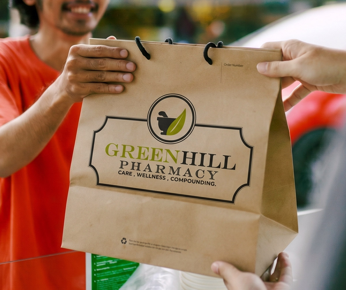 Hands passing a Greenhill Pharmacy delivery bag